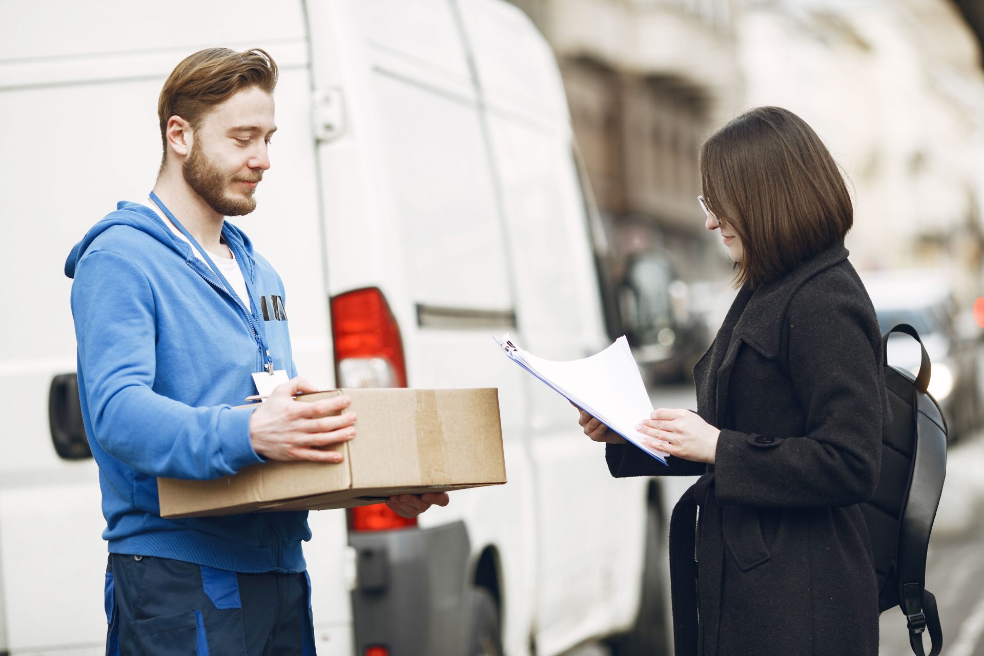 Ein Kurier übergibt einer Kundin auf einer Straße in der Stadt ein Paket und wickelt so die Zustellung ab.